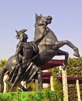 A large, dark metallic sculpture of a person riding a rearing horse.